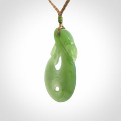 Hand carved New Zealand Inanga jade manaia with koru pendant. Carved from beautiful New Zealand Jade for NZ Pacific by Ross Crump. Unique jade jewellery for sale online. Provided with an adjustable tan cord.