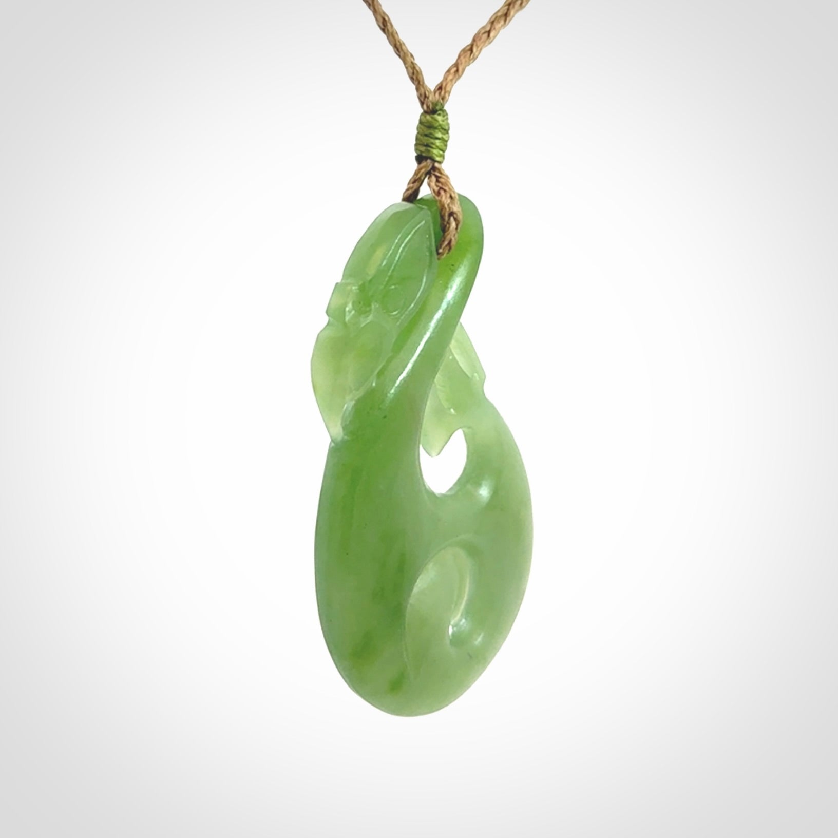 Hand carved New Zealand Inanga jade manaia with koru pendant. Carved from beautiful New Zealand Jade for NZ Pacific by Ross Crump. Unique jade jewellery for sale online. Provided with an adjustable tan cord.