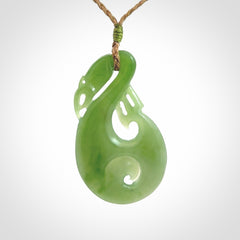 Hand carved New Zealand Inanga jade manaia with koru pendant. Carved from beautiful New Zealand Jade for NZ Pacific by Ross Crump. Unique jade jewellery for sale online. Provided with an adjustable tan cord.