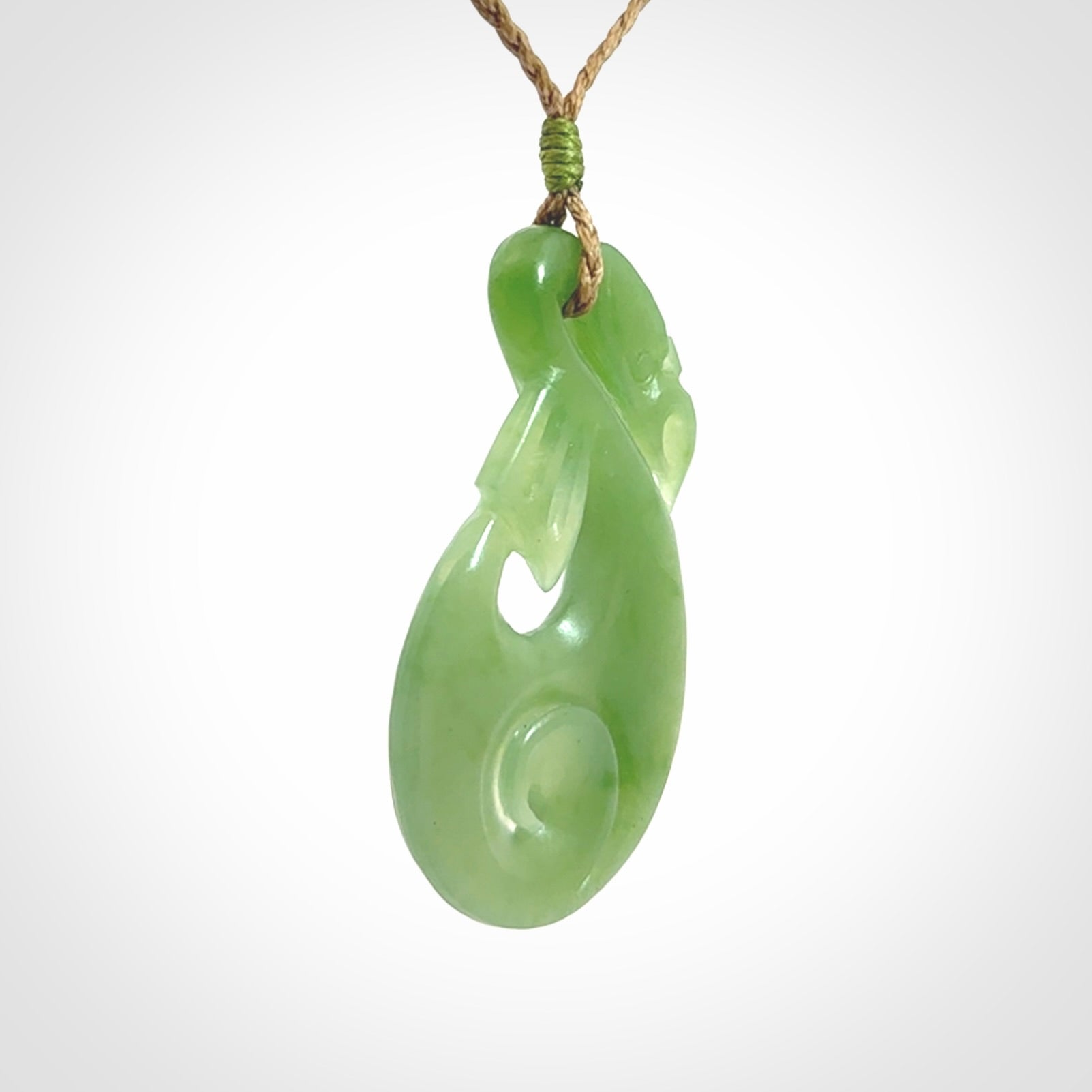 Hand carved New Zealand Inanga jade manaia with koru pendant. Carved from beautiful New Zealand Jade for NZ Pacific by Ross Crump. Unique jade jewellery for sale online. Provided with an adjustable tan cord.