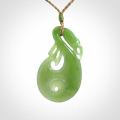 Hand carved New Zealand Inanga jade manaia with koru pendant. Carved from beautiful New Zealand Jade for NZ Pacific by Ross Crump. Unique jade jewellery for sale online. Provided with an adjustable tan cord.