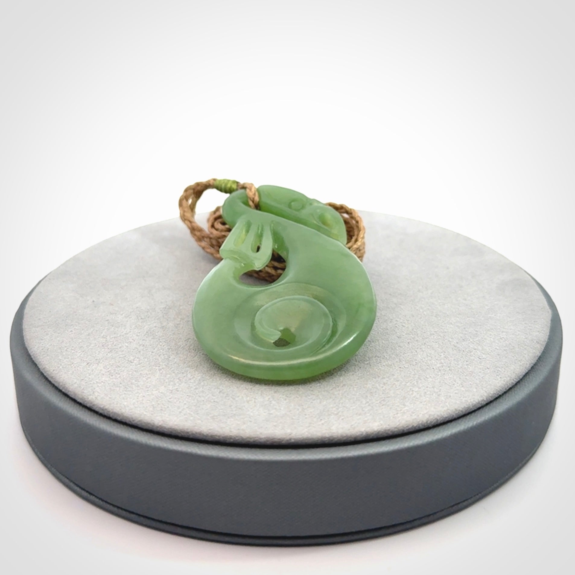 Hand carved New Zealand Inanga jade manaia with koru pendant. Carved from beautiful New Zealand Jade for NZ Pacific by Ross Crump. Unique jade jewellery for sale online. Provided with an adjustable tan cord.