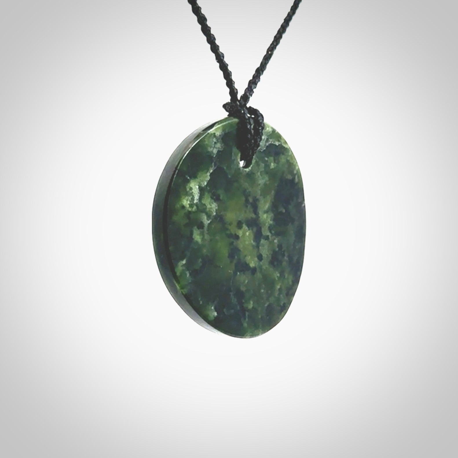 A lovely disc design with cupping on one side and the lightly convex form on the other - a little feature that captures the light and gives the piece a sense of movement and form. Hand made from New Zealand Jade by Ric Moor. Delivered with an adjustable black cord.
