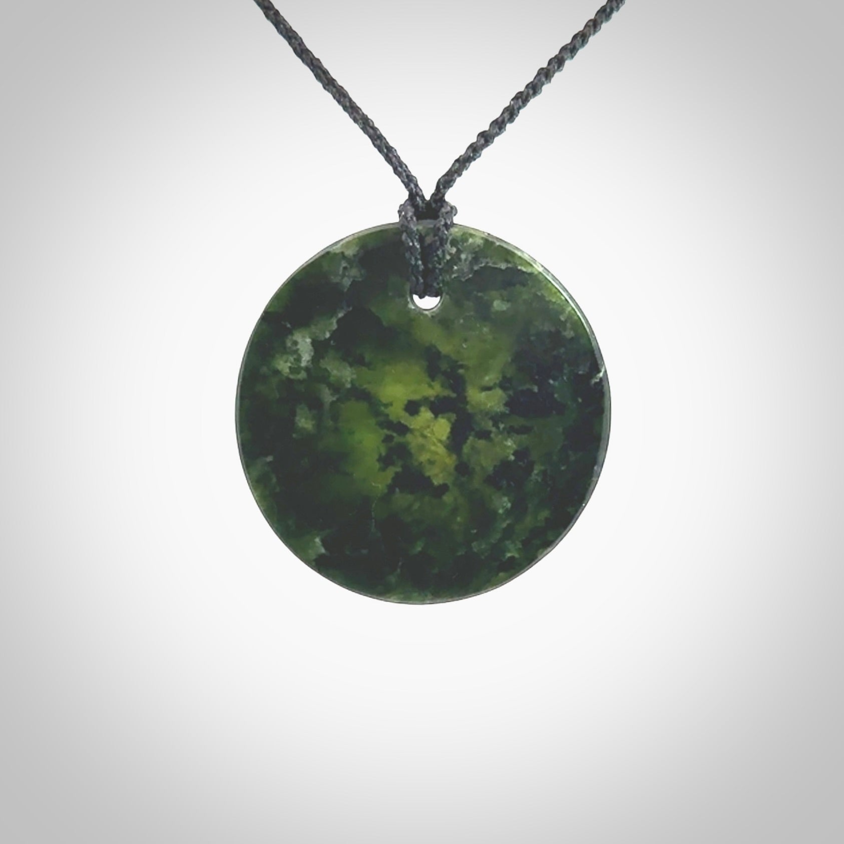 A lovely disc design with cupping on one side and the lightly convex form on the other - a little feature that captures the light and gives the piece a sense of movement and form. Hand made from New Zealand Jade by Ric Moor. Delivered with an adjustable black cord.