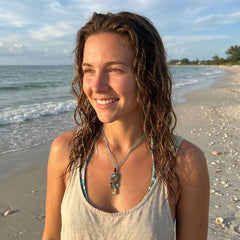 Woman with wet hair standing on a beach with ocean in the background wearing a seahorse pendant