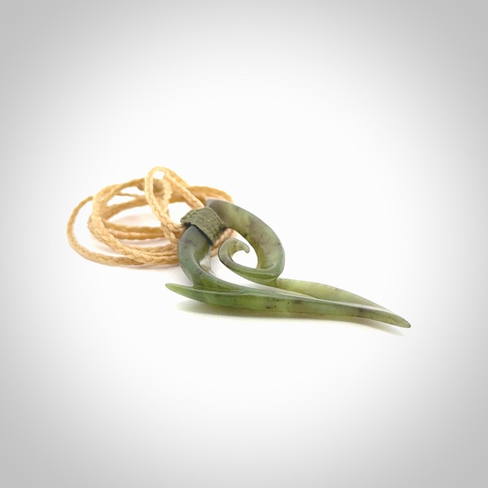 This photo shows a koru pendant carved from New Zealand Jade. We provide this piece with an adjustable oat coloured cord.