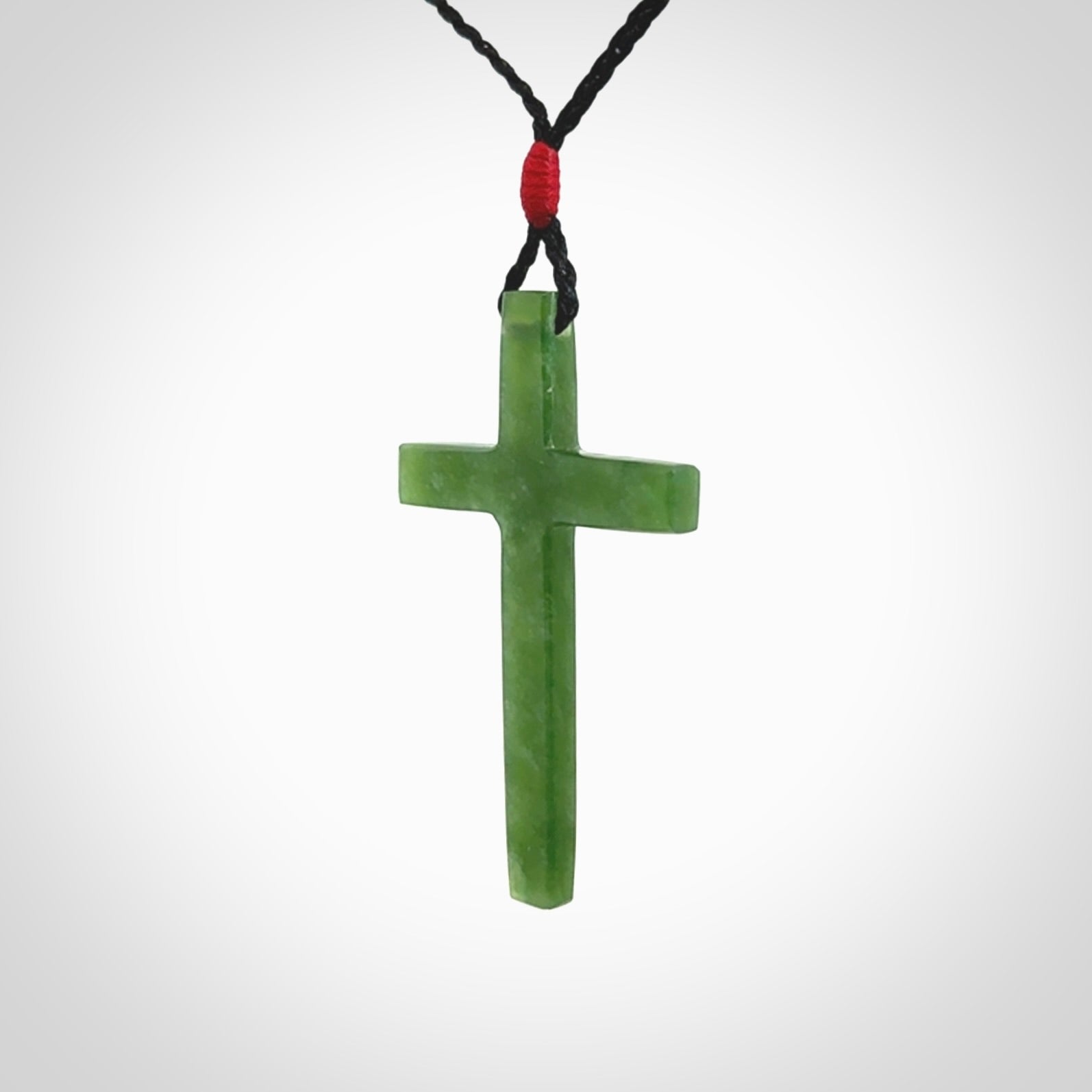 Hand carved jade cross. Made from New Zealand jade. Christian cross for sale online.This picture shows a green jade cross suspended on a fine, plaited cord. The cross is hand carved jade cross. Made from New Zealand jade. Christian cross for sale online.