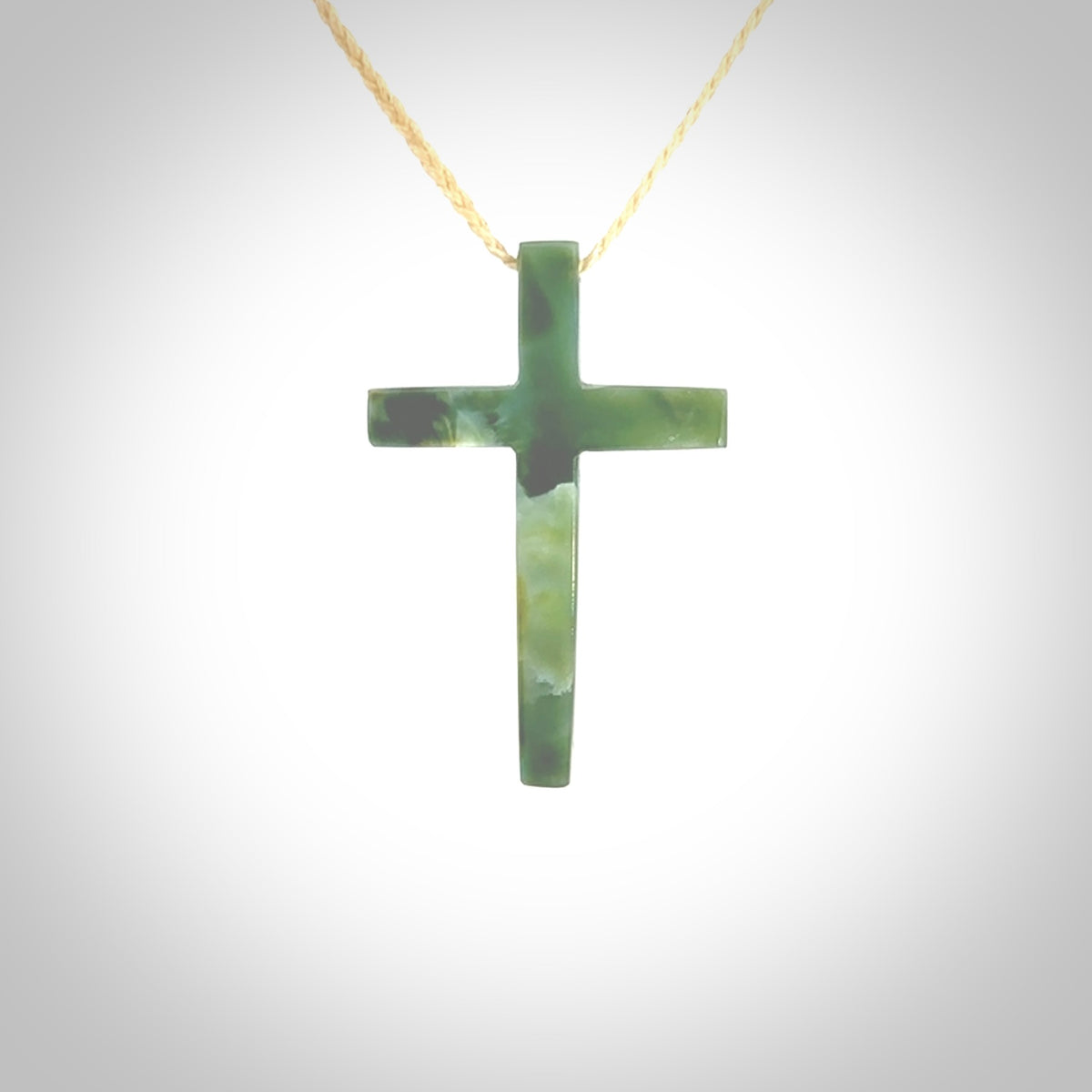 Hand carved jade cross. Made from New Zealand jade. Christian cross for sale online.This picture shows a green jade cross suspended on a fine, plaited cord. The cross is hand carved jade cross. Made from New Zealand jade. Christian cross for sale online.