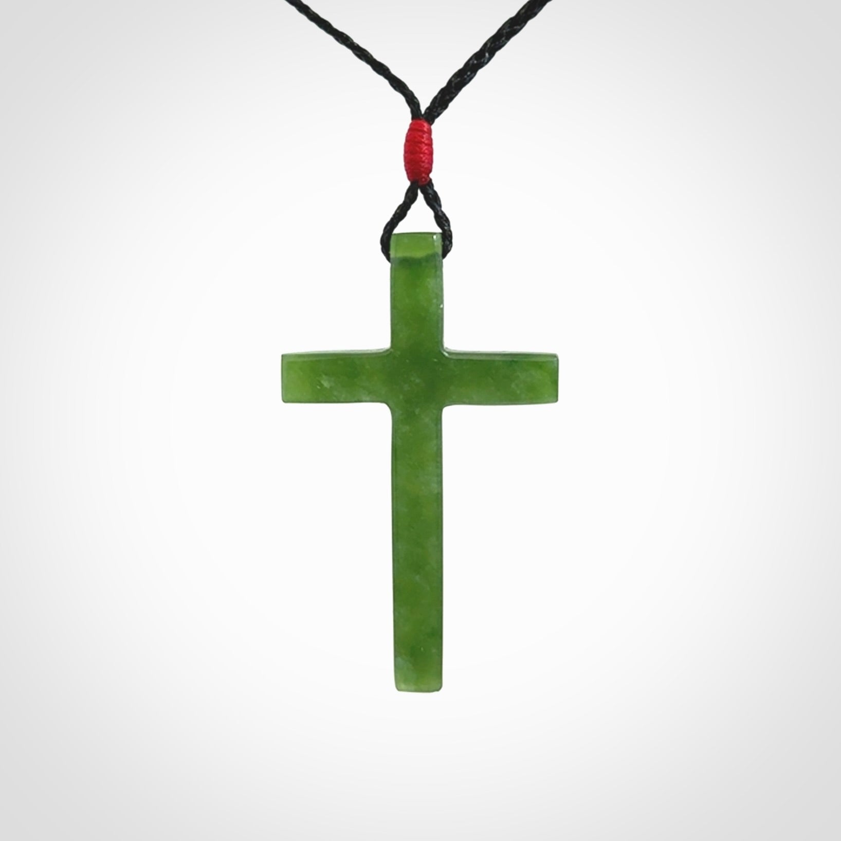 Hand carved jade cross. Made from New Zealand jade. Christian cross for sale online.This picture shows a green jade cross suspended on a fine, plaited cord. The cross is hand carved jade cross. Made from New Zealand jade. Christian cross for sale online.