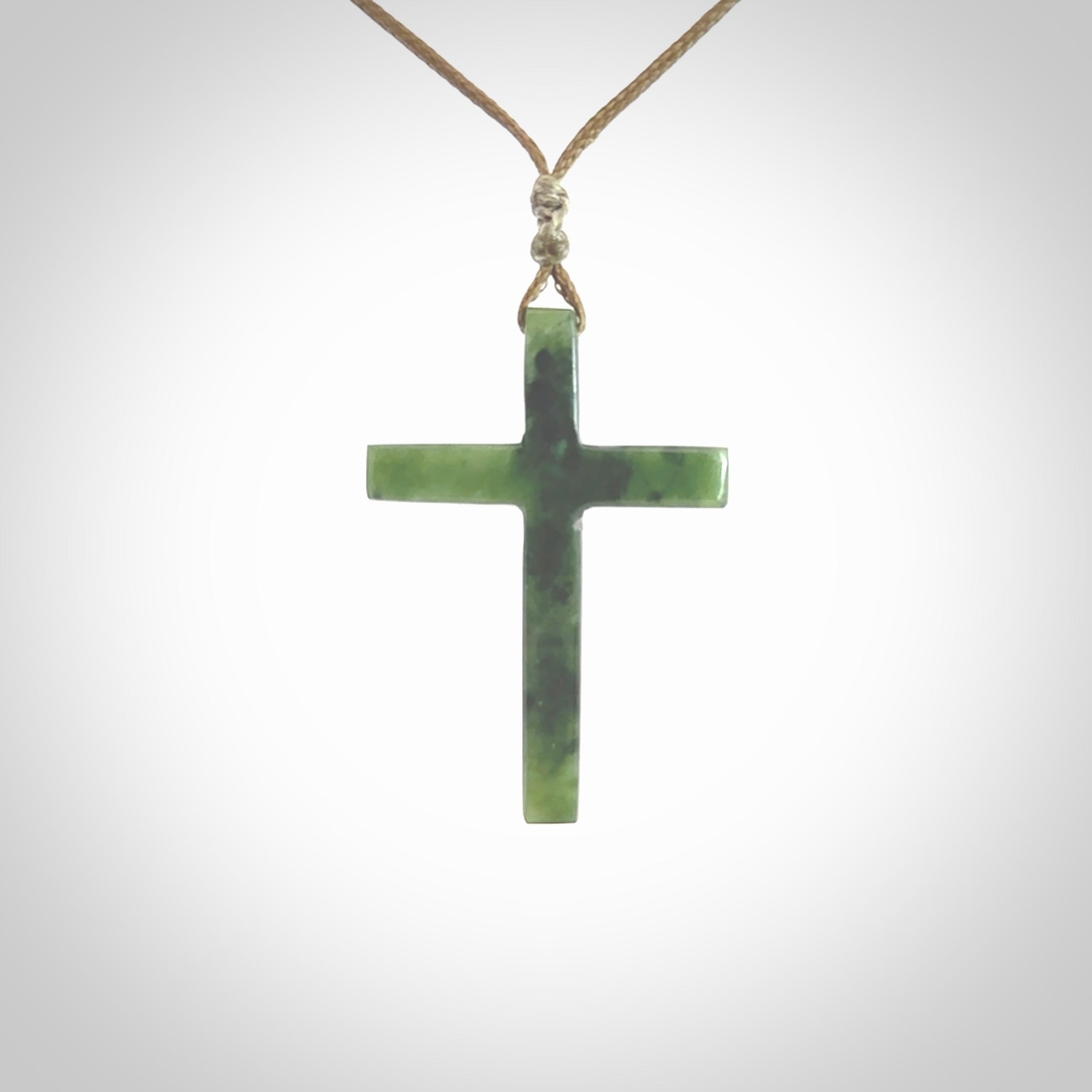 Hand carved jade cross. Made from New Zealand jade. Christian cross for sale online.This picture shows a green jade cross suspended on a fine, plaited cord. The cross is hand carved jade cross. Made from New Zealand jade. Christian cross for sale online.