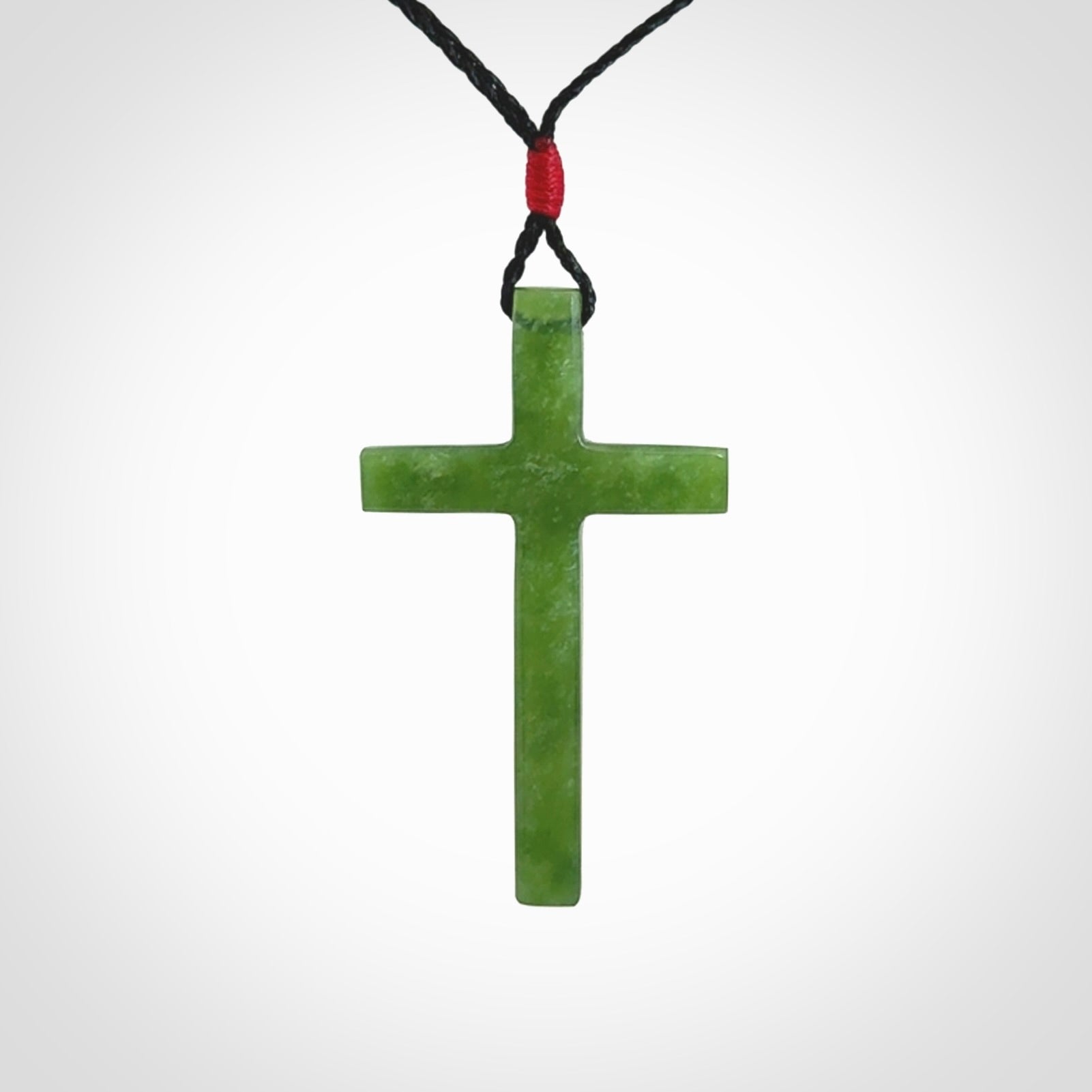 Hand carved jade cross. Made from New Zealand jade. Christian cross for sale online.This picture shows a green jade cross suspended on a fine, plaited cord. The cross is hand carved jade cross. Made from New Zealand jade. Christian cross for sale online.