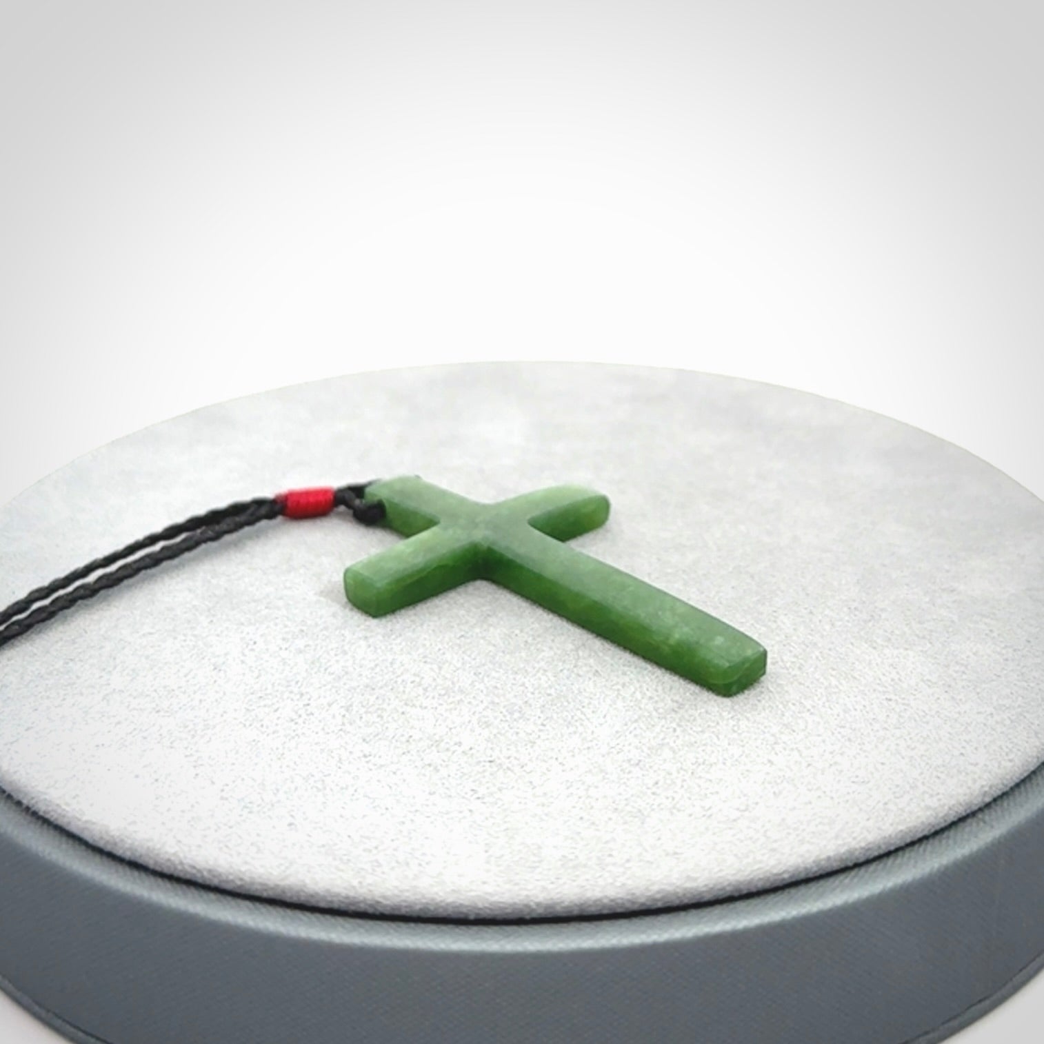 Hand carved jade cross. Made from New Zealand jade. Christian cross for sale online.This picture shows a green jade cross suspended on a fine, plaited cord. The cross is hand carved jade cross. Made from New Zealand jade. Christian cross for sale online.