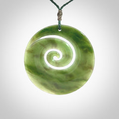This picture shows a large hand-carved koru. It is carved from British Columbian jade and is suspended from a hand-plaited, green cord.