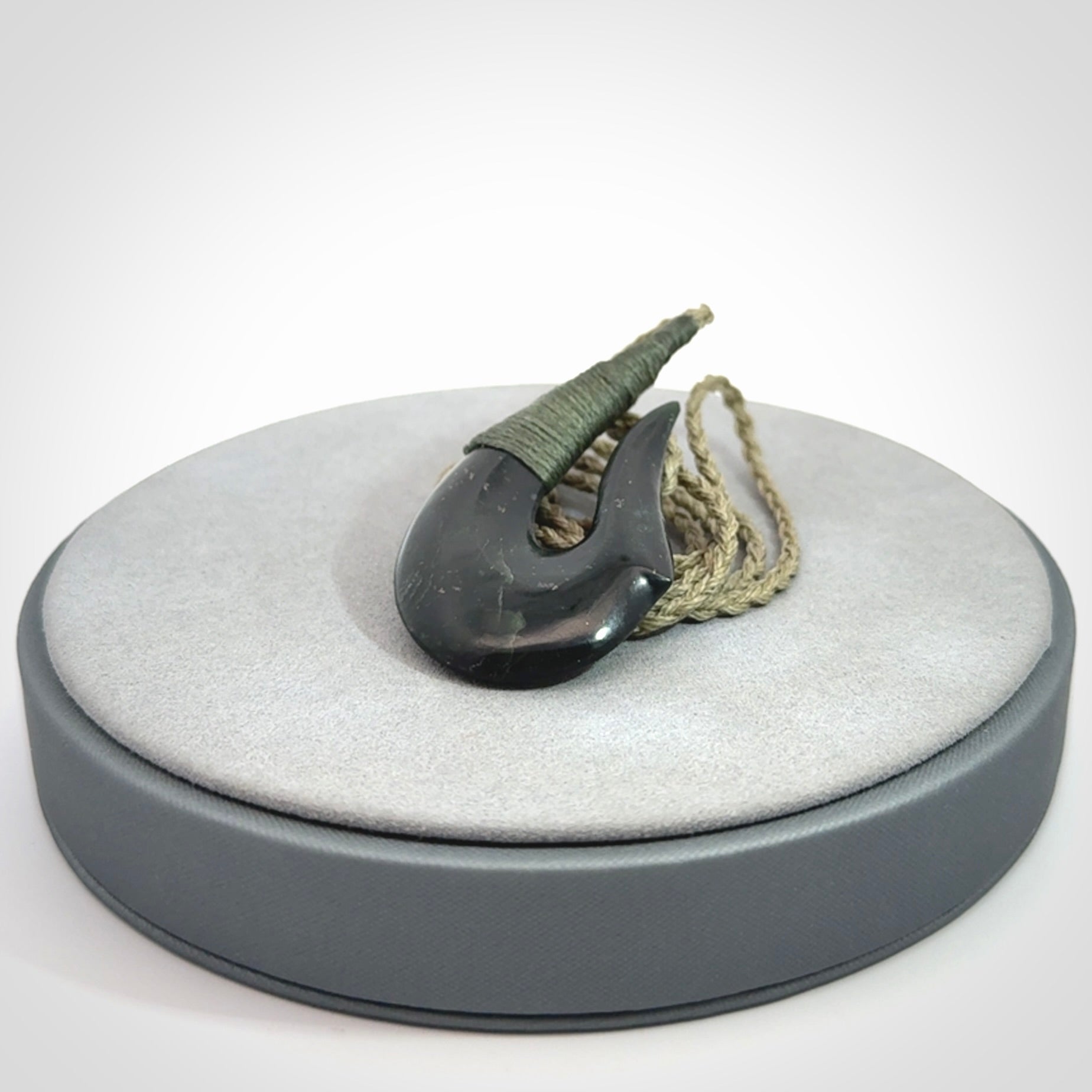 This photo shows a New Zealand Tangiwai hook, or matau, pendant. The plaited cord is khaki and the length can be adjusted.