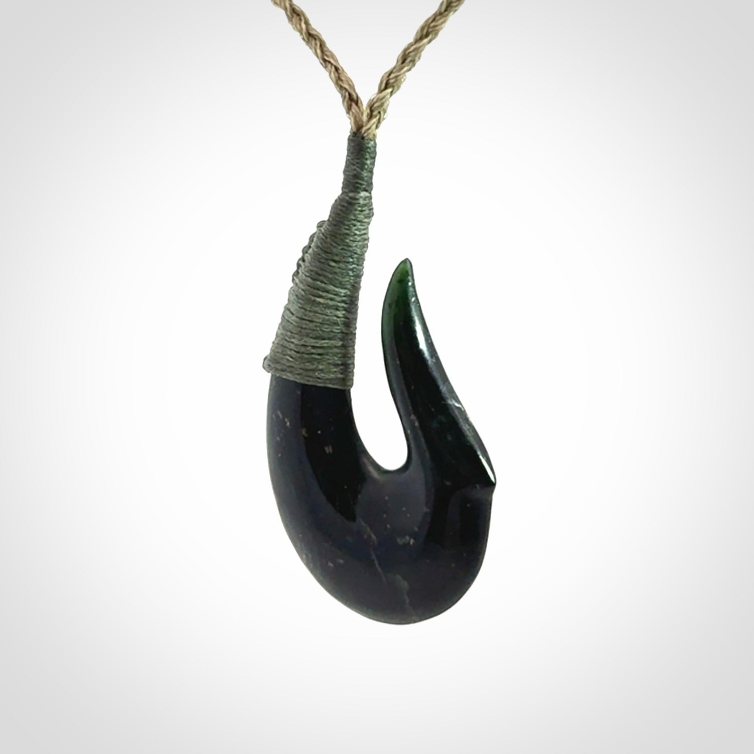 This photo shows a New Zealand Tangiwai hook, or matau, pendant. The plaited cord is khaki and the length can be adjusted.
