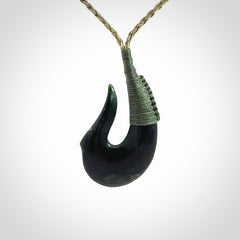 This photo shows a New Zealand Tangiwai hook, or matau, pendant. The plaited cord is khaki and the length can be adjusted.