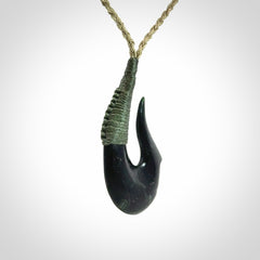 This photo shows a New Zealand Tangiwai hook, or matau, pendant. The plaited cord is khaki and the length can be adjusted.