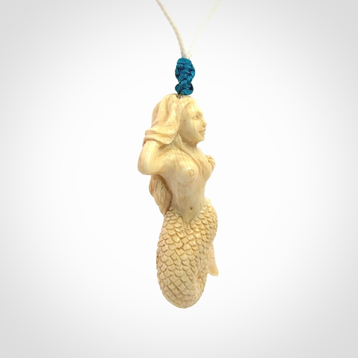This photo shows a photo of a mermaid pendant. It is handcarved from a beautifully creamy piece of woolly mammoth tusk. It is suspended on an adjustable cord.