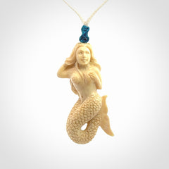 This photo shows a photo of a mermaid pendant. It is handcarved from a beautifully creamy piece of woolly mammoth tusk. It is suspended on an adjustable cord.