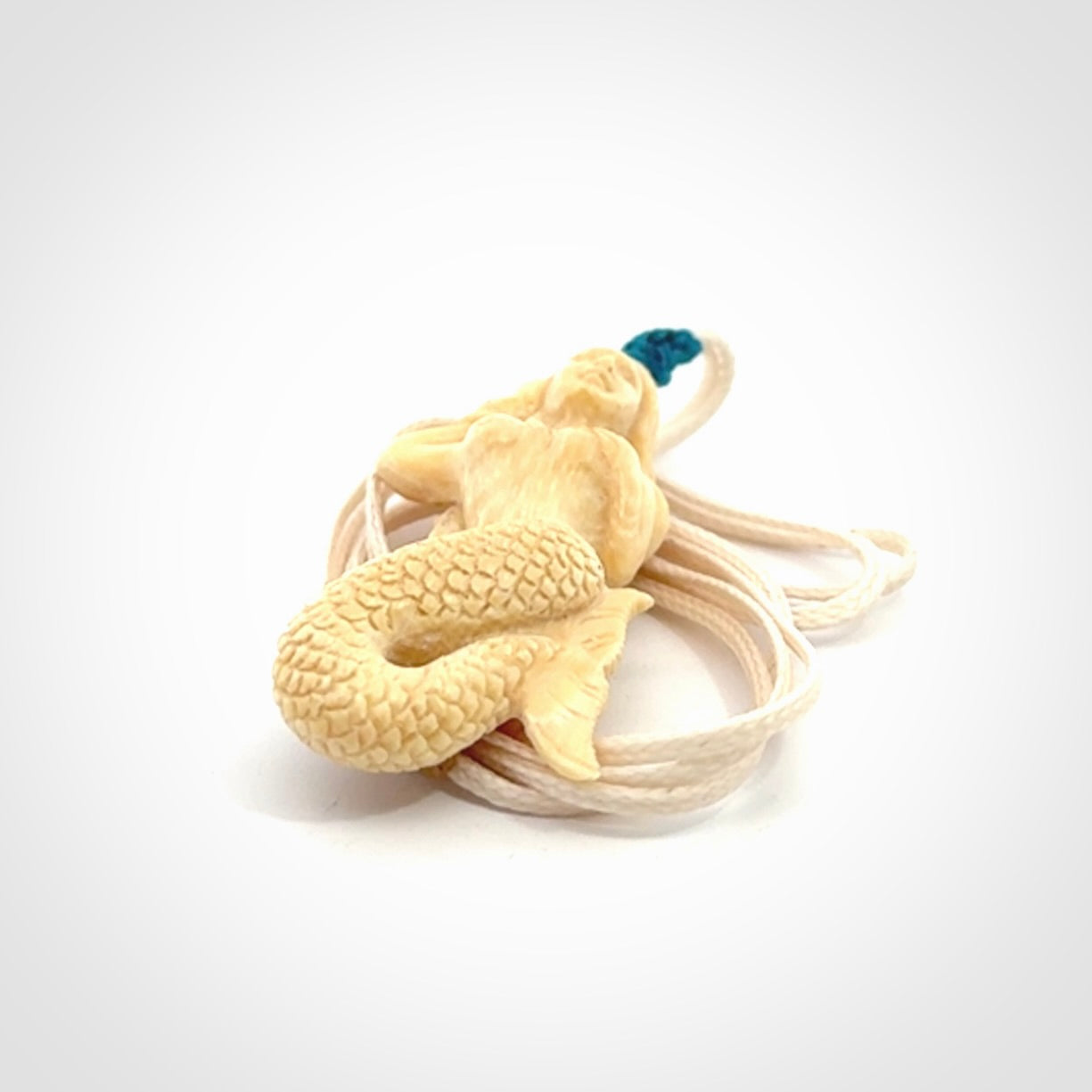 This photo shows a photo of a mermaid pendant. It is handcarved from a beautifully creamy piece of woolly mammoth tusk. It is suspended on an adjustable cord.