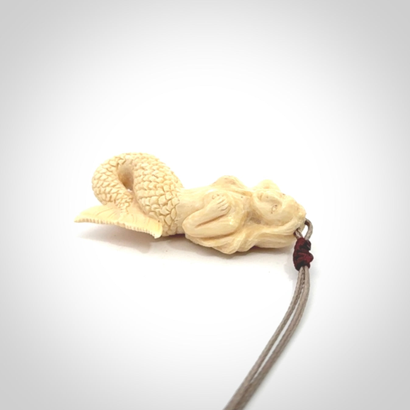 This photo shows a photo of a mermaid pendant. It is handcarved from a beautifully creamy piece of woolly mammoth tusk. It is suspended on an adjustable cord.