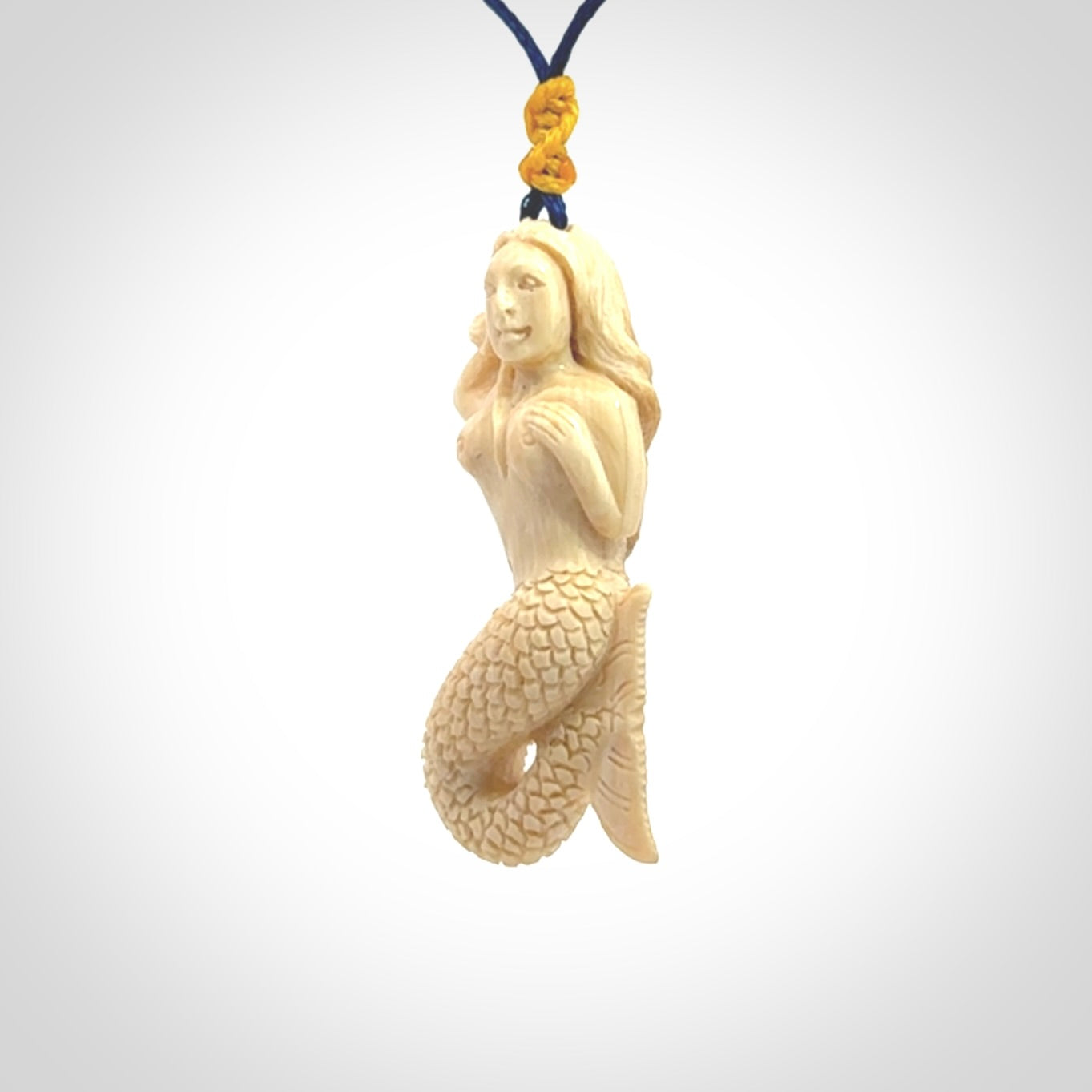 This photo shows a photo of a mermaid pendant. It is handcarved from a beautifully creamy piece of woolly mammoth tusk. It is suspended on an adjustable cord.