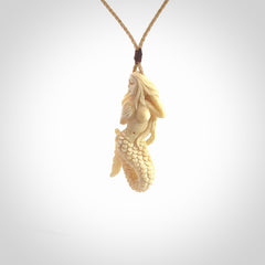 This photo shows a photo of a mermaid pendant. It is handcarved from a beautifully creamy piece of woolly mammoth tusk. It is suspended on an adjustable cord.
