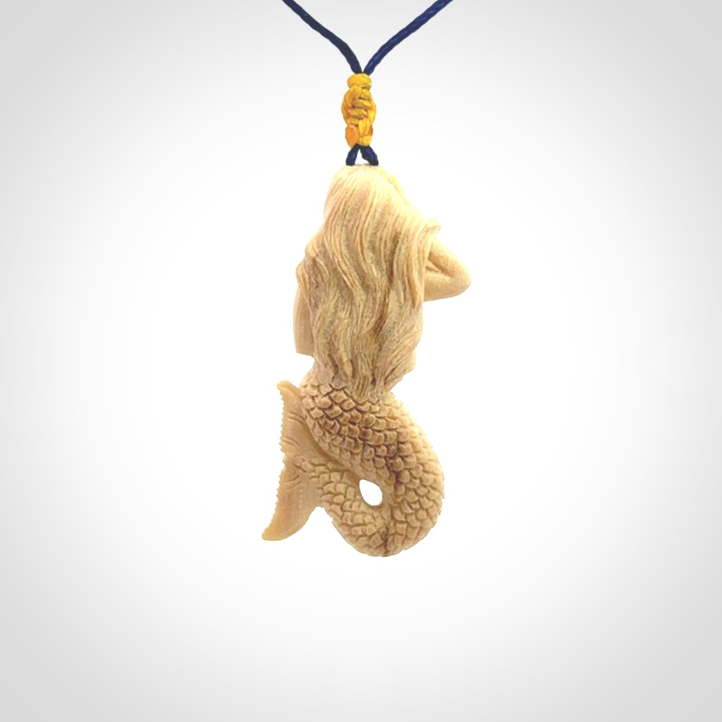 This photo shows a photo of a mermaid pendant. It is handcarved from a beautifully creamy piece of woolly mammoth tusk. It is suspended on an adjustable cord.