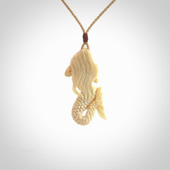 This photo shows a photo of a mermaid pendant. It is handcarved from a beautifully creamy piece of woolly mammoth tusk. It is suspended on an adjustable cord.