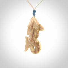 This photo shows a photo of a mermaid pendant. It is handcarved from a beautifully creamy piece of woolly mammoth tusk. It is suspended on an adjustable cord.