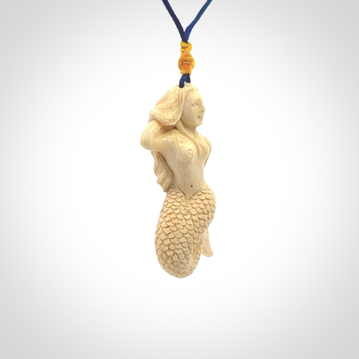 This photo shows a photo of a mermaid pendant. It is handcarved from a beautifully creamy piece of woolly mammoth tusk. It is suspended on an adjustable cord.