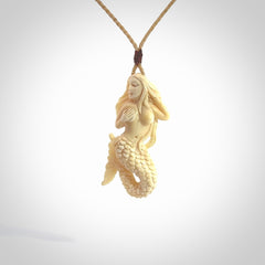 This photo shows a photo of a mermaid pendant. It is handcarved from a beautifully creamy piece of woolly mammoth tusk. It is suspended on an adjustable cord.