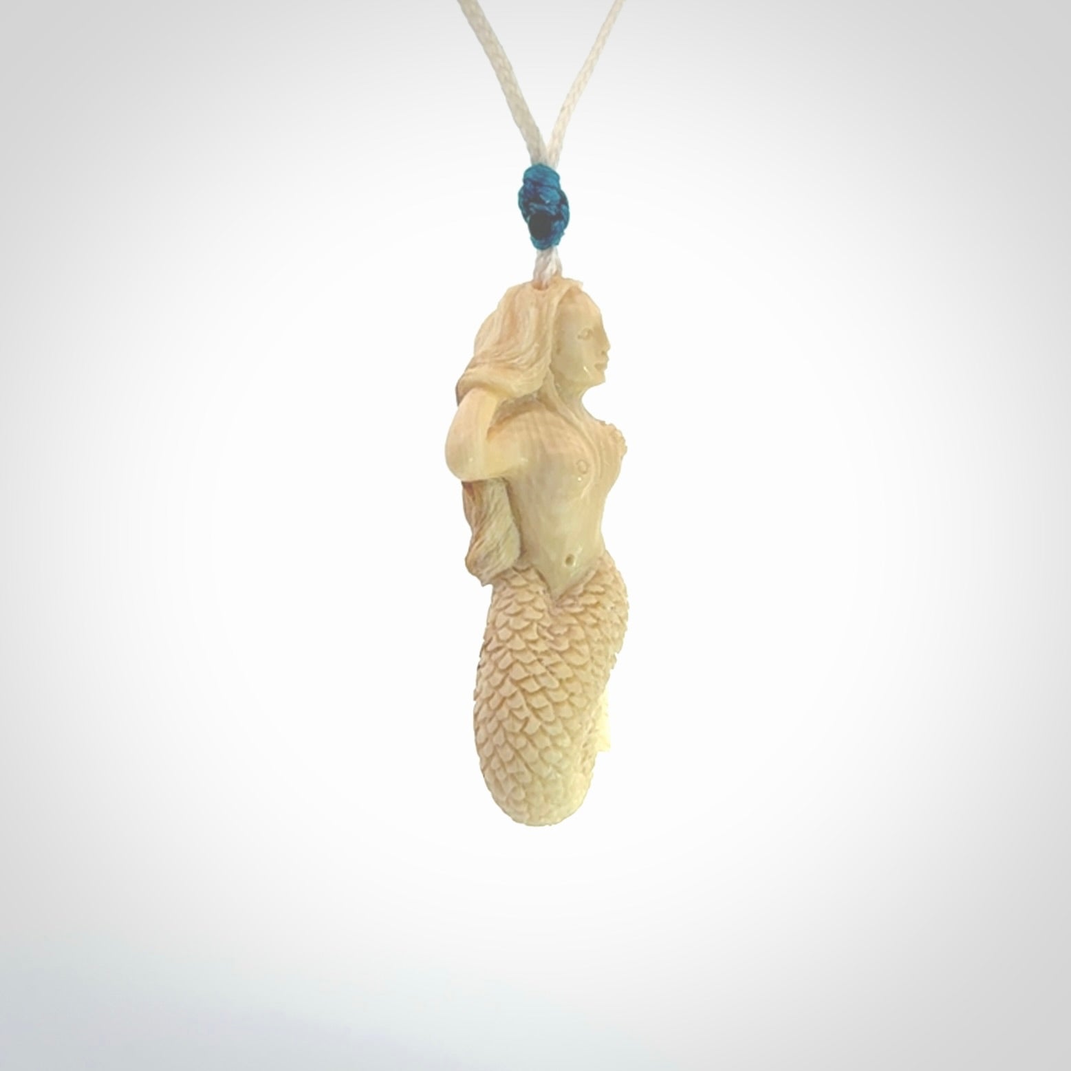 This photo shows a photo of a mermaid pendant. It is handcarved from a beautifully creamy piece of woolly mammoth tusk. It is suspended on an adjustable cord.