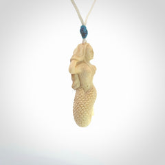 This photo shows a photo of a mermaid pendant. It is handcarved from a beautifully creamy piece of woolly mammoth tusk. It is suspended on an adjustable cord.
