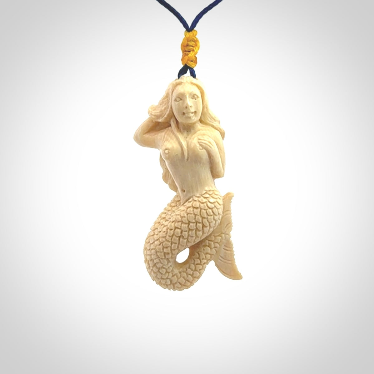 This photo shows a photo of a mermaid pendant. It is handcarved from a beautifully creamy piece of woolly mammoth tusk. It is suspended on an adjustable cord.