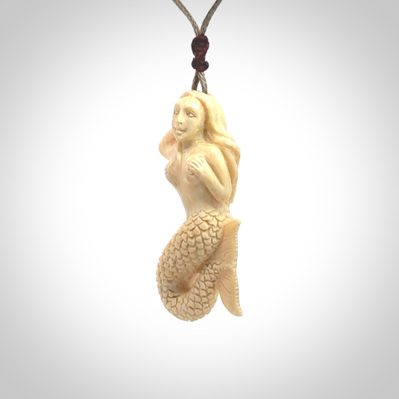 This photo shows a photo of a mermaid pendant. It is handcarved from a beautifully creamy piece of woolly mammoth tusk. It is suspended on an adjustable cord.