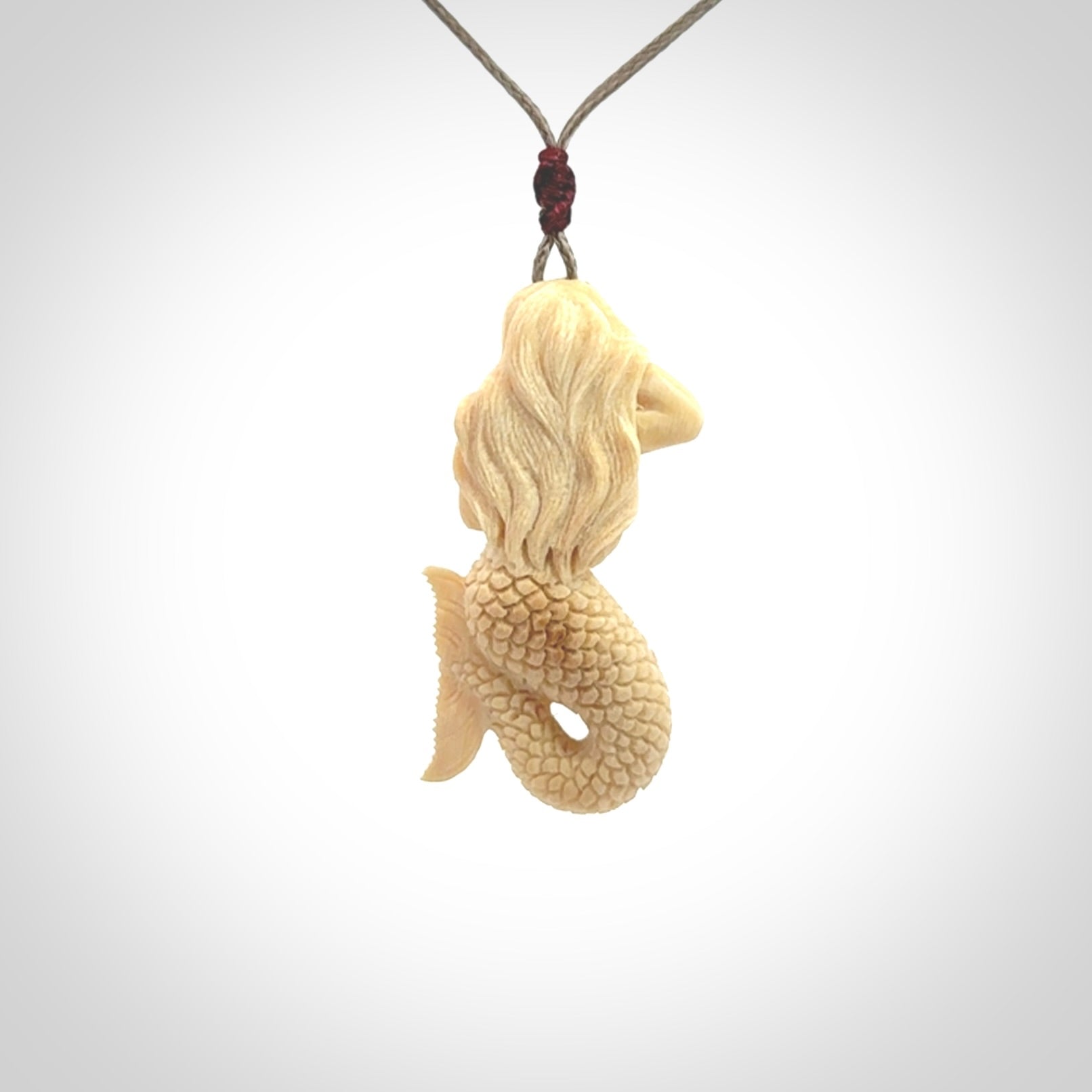 This photo shows a photo of a mermaid pendant. It is handcarved from a beautifully creamy piece of woolly mammoth tusk. It is suspended on an adjustable cord.