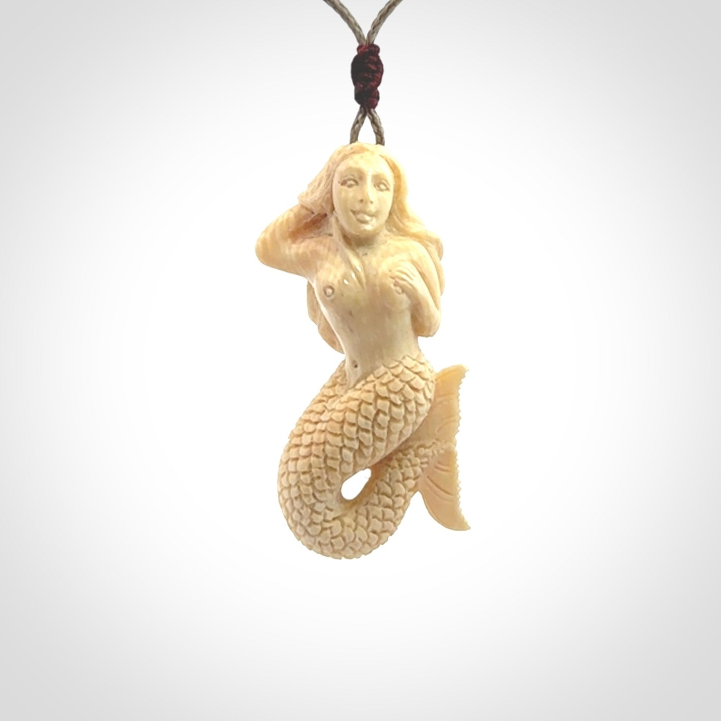 This photo shows a photo of a mermaid pendant. It is handcarved from a beautifully creamy piece of woolly mammoth tusk. It is suspended on an adjustable cord.