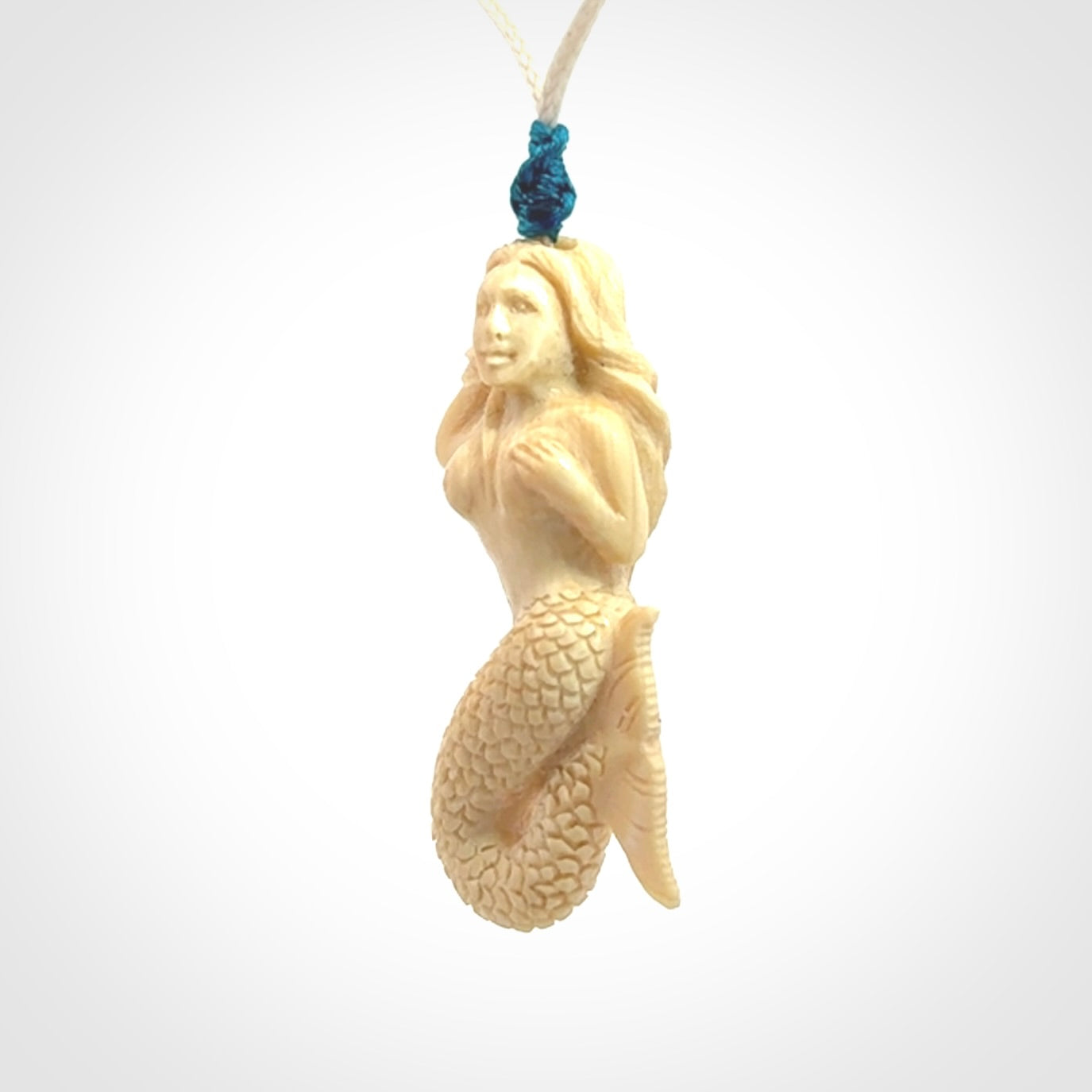 This photo shows a photo of a mermaid pendant. It is handcarved from a beautifully creamy piece of woolly mammoth tusk. It is suspended on an adjustable cord.