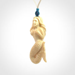 This photo shows a photo of a mermaid pendant. It is handcarved from a beautifully creamy piece of woolly mammoth tusk. It is suspended on an adjustable cord.