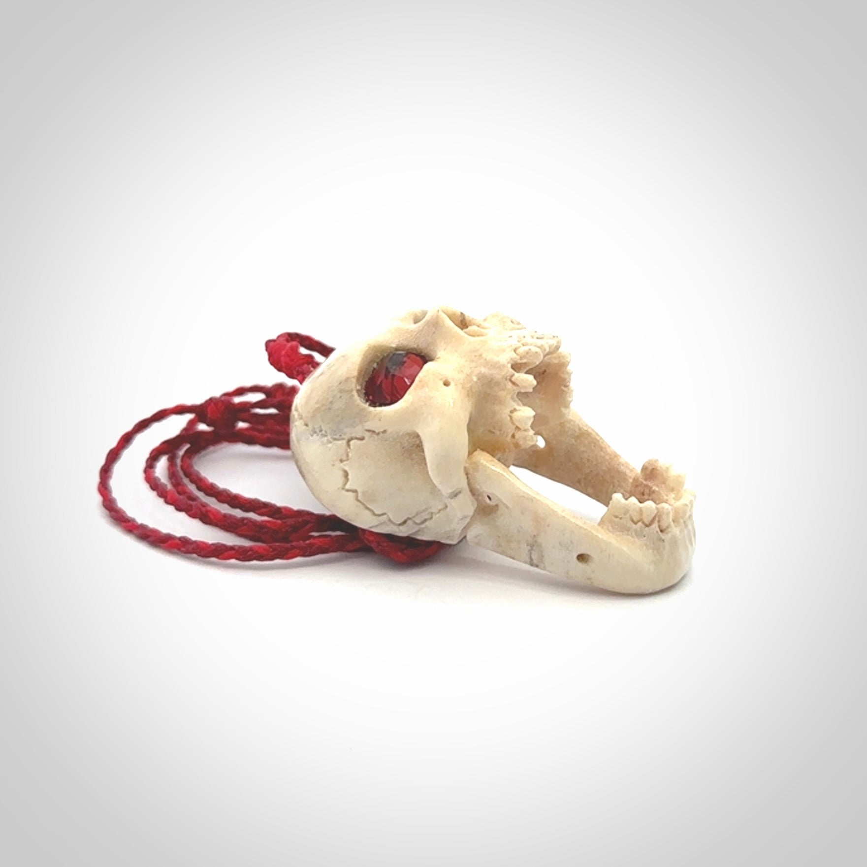 A hand carved SKULL pendant made from deer antler with Pyrope Garnet eyes. This is a work of art carved in deer antler, bone. We deliver this pendant to you on a plaited juicy red and passion red cord. Delivery with Express Courier is included in the price.