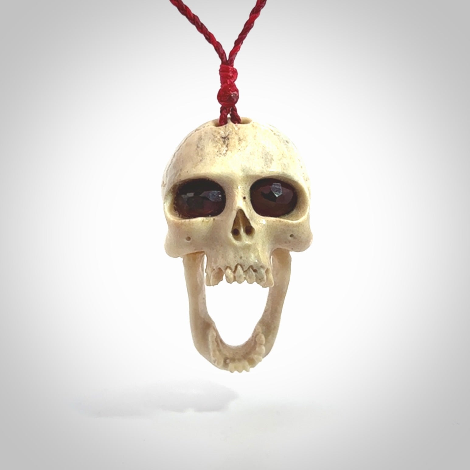 A hand carved SKULL pendant made from deer antler with Pyrope Garnet eyes. This is a work of art carved in deer antler, bone. We deliver this pendant to you on a plaited juicy red and passion red cord. Delivery with Express Courier is included in the price.