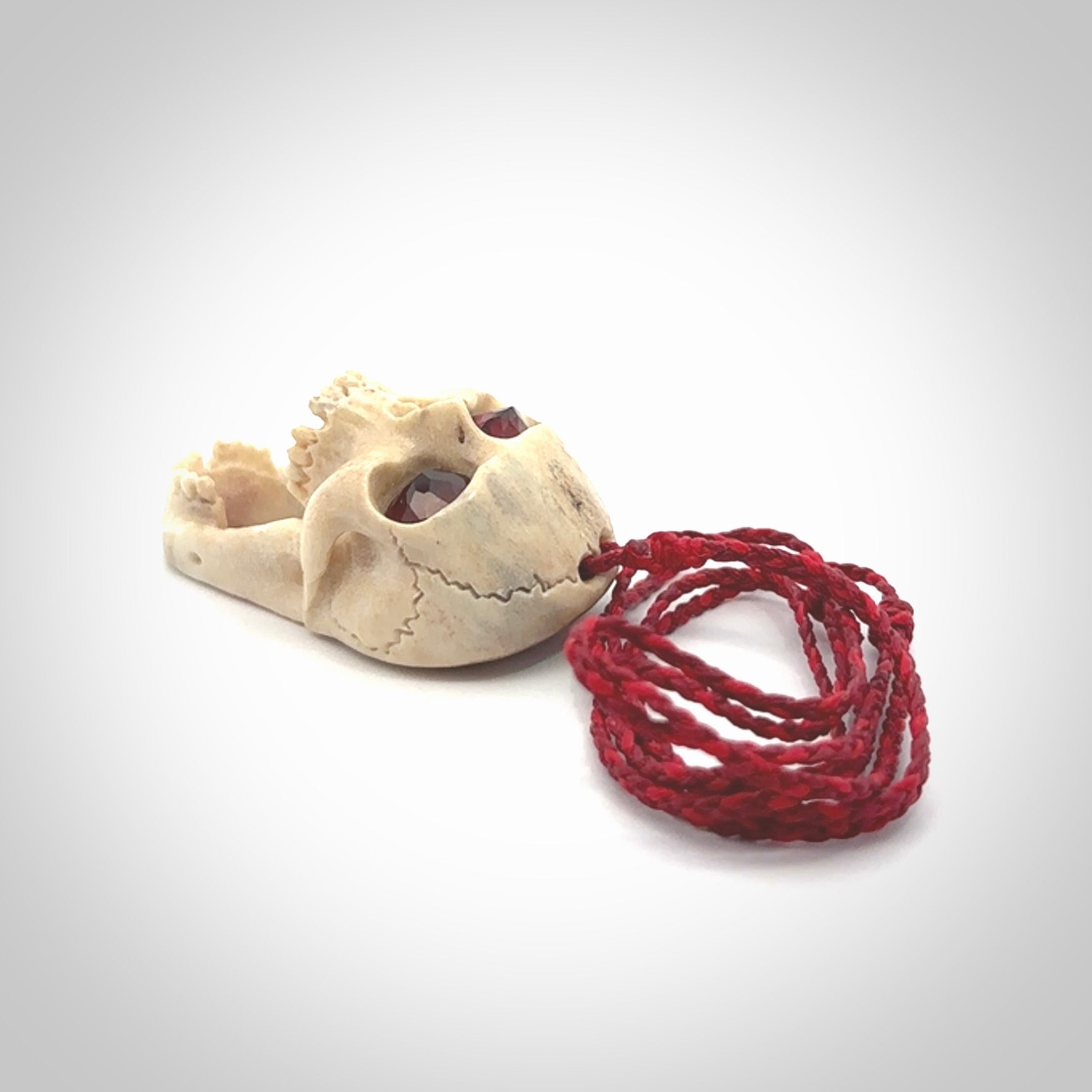 A hand carved SKULL pendant made from deer antler with Pyrope Garnet eyes. This is a work of art carved in deer antler, bone. We deliver this pendant to you on a plaited juicy red and passion red cord. Delivery with Express Courier is included in the price.