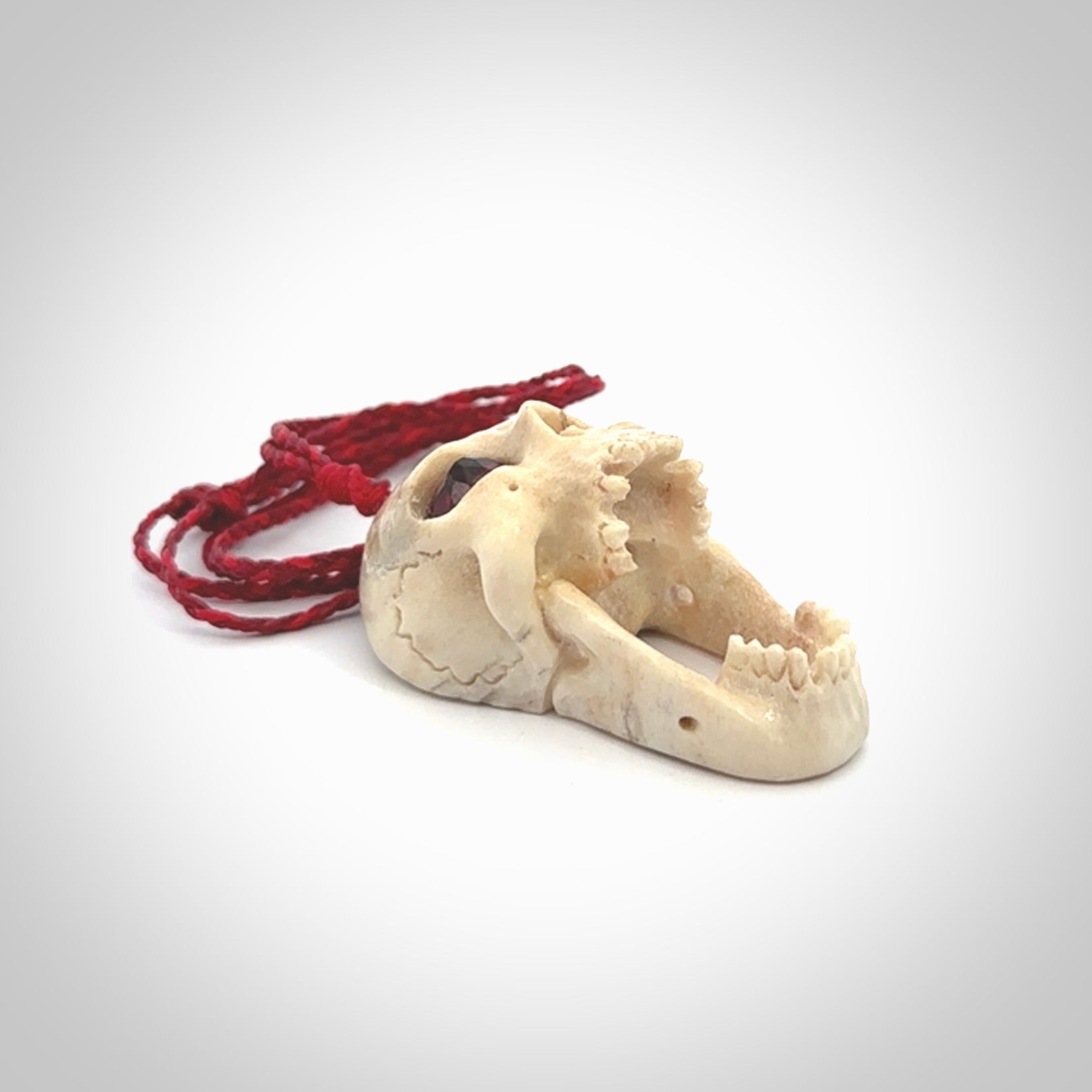 A hand carved SKULL pendant made from deer antler with Pyrope Garnet eyes. This is a work of art carved in deer antler, bone. We deliver this pendant to you on a plaited juicy red and passion red cord. Delivery with Express Courier is included in the price.