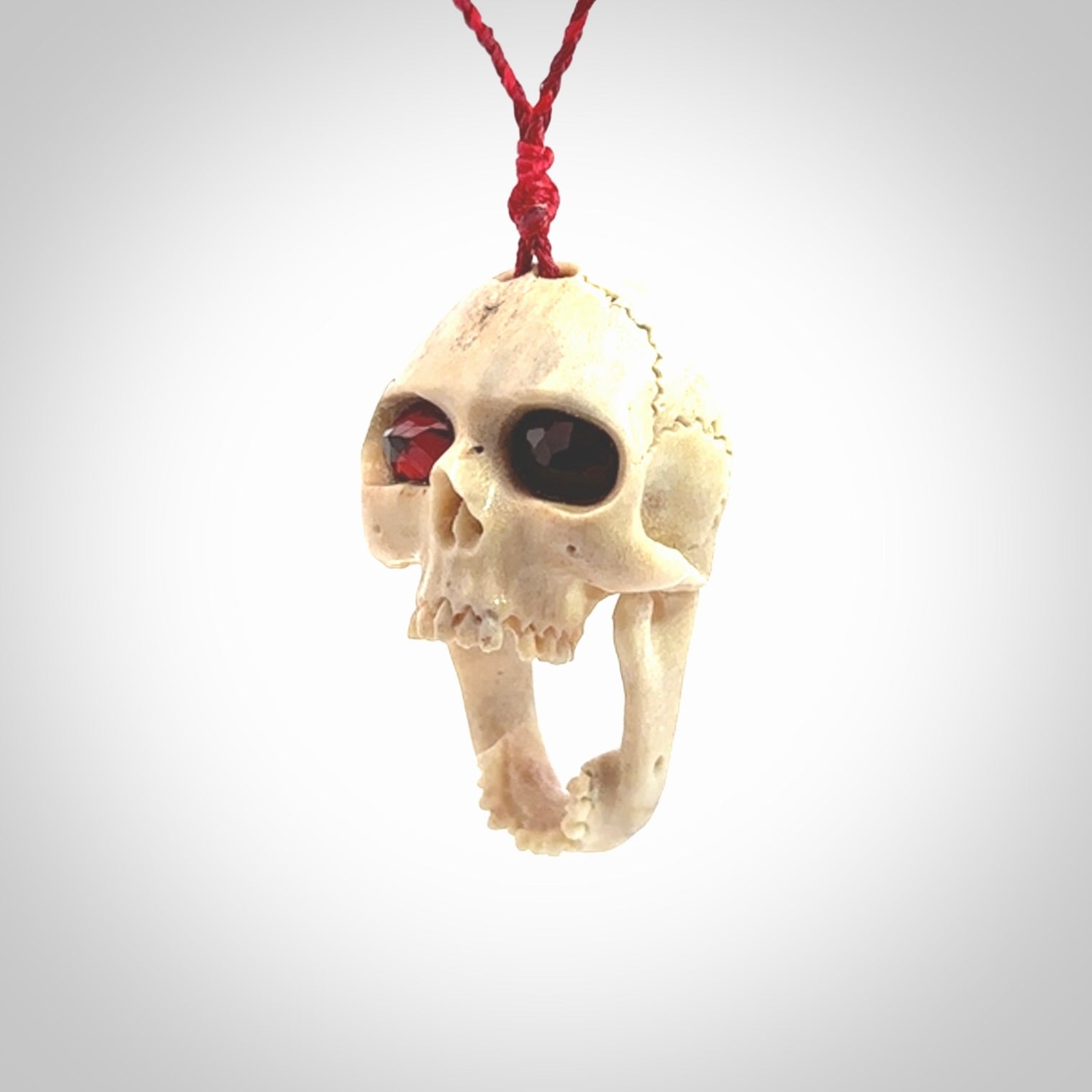 A hand carved SKULL pendant made from deer antler with Pyrope Garnet eyes. This is a work of art carved in deer antler, bone. We deliver this pendant to you on a plaited juicy red and passion red cord. Delivery with Express Courier is included in the price.