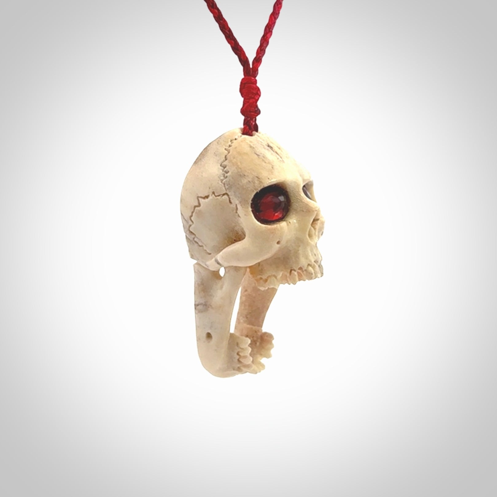 A hand carved SKULL pendant made from deer antler with Pyrope Garnet eyes. This is a work of art carved in deer antler, bone. We deliver this pendant to you on a plaited juicy red and passion red cord. Delivery with Express Courier is included in the price.