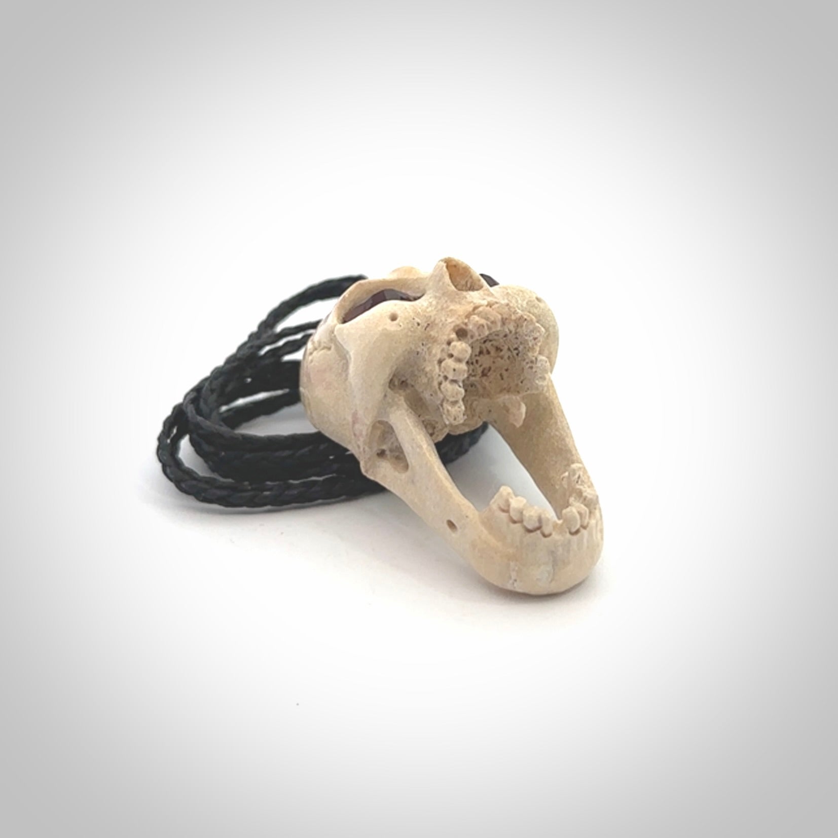 A hand carved SKULL pendant made from deer antler with Pyrope Garnet eyes. This is a work of art carved in deer antler, bone. We deliver this pendant to you on a plaited black cord. Delivery with Express Courier is included in the price.