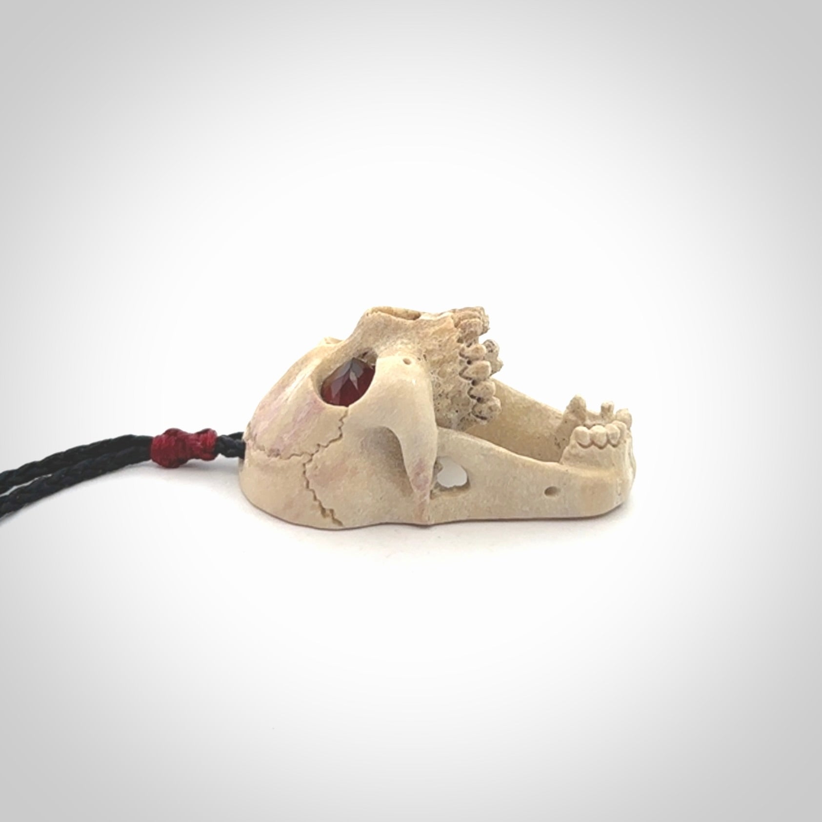 A hand carved SKULL pendant made from deer antler with Pyrope Garnet eyes. This is a work of art carved in deer antler, bone. We deliver this pendant to you on a plaited black cord. Delivery with Express Courier is included in the price.