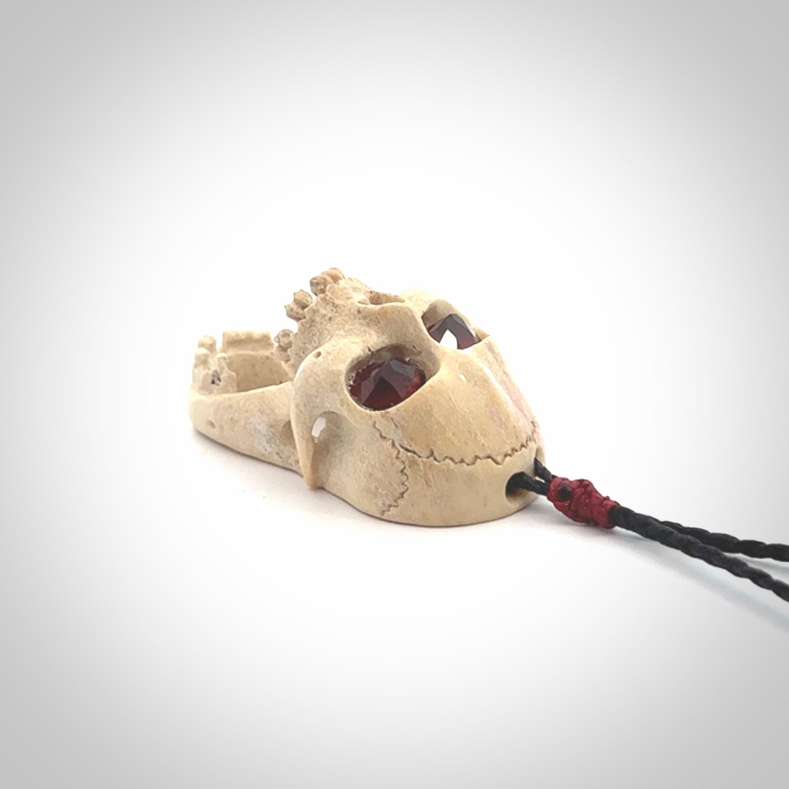 A hand carved SKULL pendant made from deer antler with Pyrope Garnet eyes. This is a work of art carved in deer antler, bone. We deliver this pendant to you on a plaited black cord. Delivery with Express Courier is included in the price.