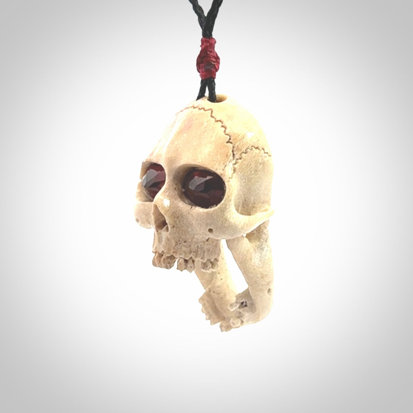 A hand carved SKULL pendant made from deer antler with Pyrope Garnet eyes. This is a work of art carved in deer antler, bone. We deliver this pendant to you on a plaited black cord. Delivery with Express Courier is included in the price.